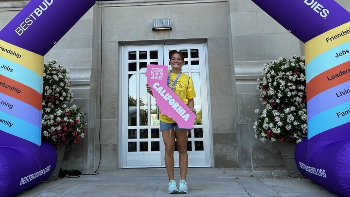 A student in a yellow shirt holds a cutout of California with a Best Buddies logo on it.