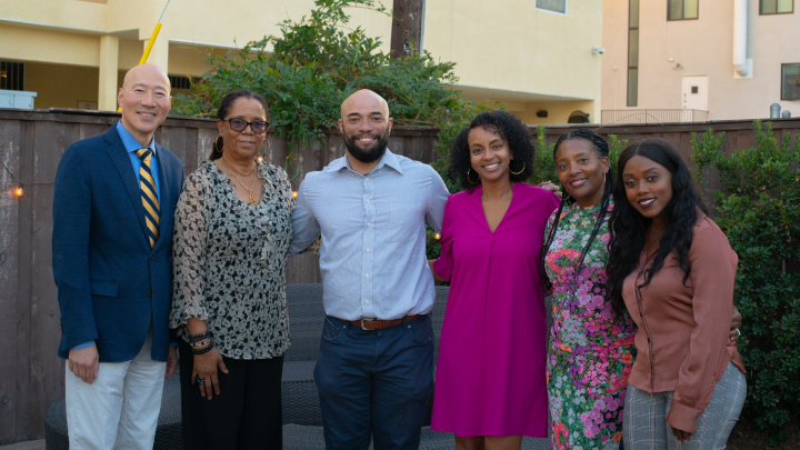 A group of six people in formal attire pose and smile in an outdoor setting.