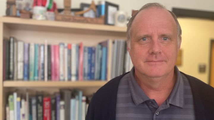 A man stands in front of a bookshelf full of journals.