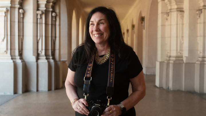 A smiling Marva Cappello holds a camera at Balboa Park.