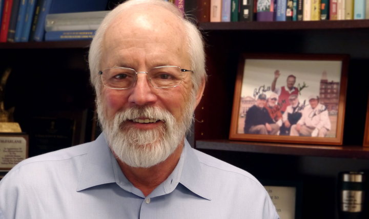 A smiling Fred McFarlane poses in front of a bookshelf.