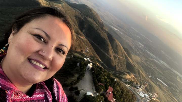 A woman smiles in a selfie taken atop a mountain.