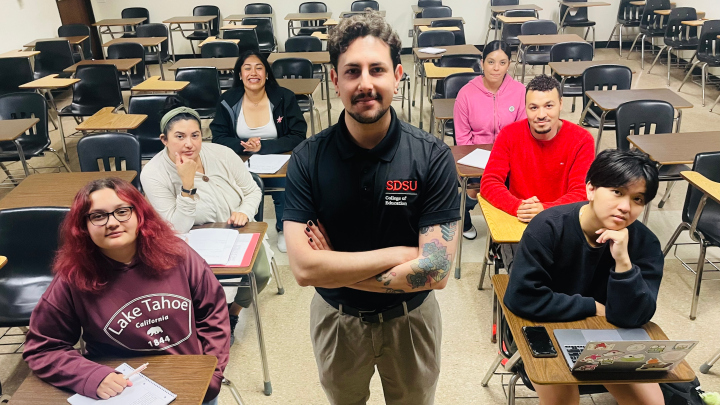 A standing instructor with six seated students in a classroom.