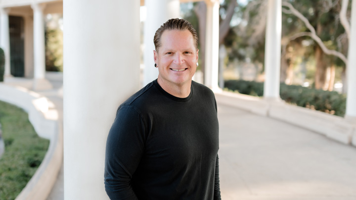 A man in black stands outside in front of white columns.
