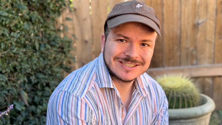 A man in a white striped shirt and brown baseball cap smiles.