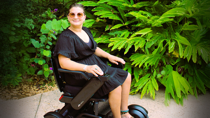 A woman in a black dress sits in a power chair.